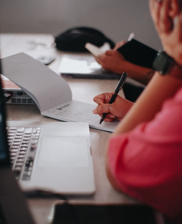 Laptop on a wooden desk next to a white chair and a mouse.